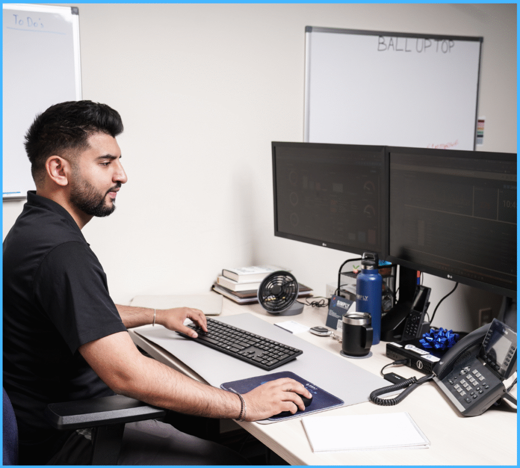 IT technician working at dual monitors in a professional office environment.